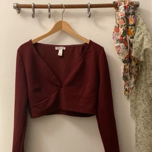 Vinröd tröja - Denne underbara utringade toppen sitter kort på kroppen med långa ärmar. Utrigningen är säkrad med en gummirand. Gott skick