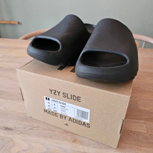 Yeezy slides svarta - Yeezy slides, svarta, inköpta förra sommaren. Bra skick(enligt bilder). Kvitto och låda medföljer. Storleken är liten så passar mer 41 än 42, men storleken är 42 enligt låda.