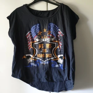 Topp, born to be wild, stl M, Ginatricot - Topp, längre tyg baktill.  Storlek: M  Mått: axelbredd ca 56cm, längd ca 49cm   Skick: begagnat skick, trycket ser sprucket ut. Men tror det är stilen.  Har blivit blekare än ny. Färg: svart med USA flagga. Örnar, text Märke: gina tricot