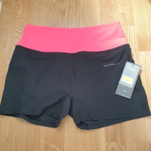 Svarta Träningsshorts, stl 42, swedemount  - Träningsshorts (short short training tights W)Märke: swedemount  Skick: ny, med prislapp  Storlek: 42  Färg: svarta med rosa kant  Matrial: 88% polyester, 12% Spandex  Köpt för 300kr.  Katt har funnits i hemmet 