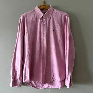 En rosa Ralph Lauren-skjorta i vävt tyg, lite lätt rosa. Den är vältillverkad och lite grövre i tyget än deras tunnare skjortor. Hjälper min sambo att sälja den 🌸