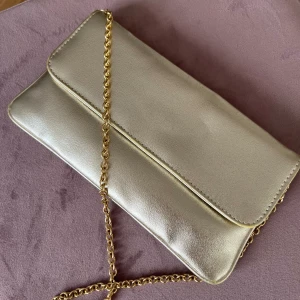 💛Guldfärgad vintage kuvertväska 💛 - Med guldpläterad kedja .  Märke: Okänt, köpt på second hand . Längd: 23 cm . Bredd: 12 cm .  Material: Okänt . Utan anmärkning men i använt skick.