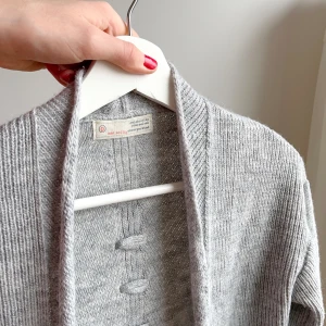 Odd Molly-kofta, grå storlek 0 - Något längre kofta från Odd Molly i storlek 0 = XS.   Finns två knappar att knäppa med - men som knappt syns när koftan är öppen.   Två fickor fram.   Fin detalj med ”flätan” på ryggen.   Väldigt bekväm.   45% akryl, 25% alpacka, 20% ull, 10% viskos.