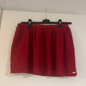 Kjol  - En söt röd kjol av spets med en liten rosett. Jätte fin på sommaren. Snygg att ha runt midjan. Helt oanvänd. Ordinarie pris 100kr