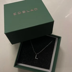 Bokstavshalsband Edblad - Jättefint bokstavshalsband från Edblad med bokstaven L💗Present som ej passade mig, helt oanvänd och har bara legat i kartongen. Smycket är silverfärgad med en berlock av fina klara stenar infattade i blankt rostfritt stål🩶