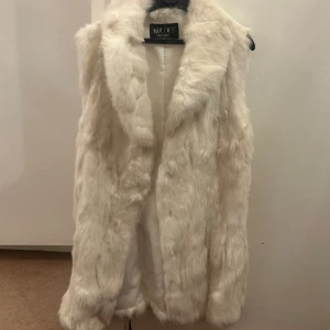 Pälsväst vit äkta  - En äkta pälsväst i vit färg från märket Hollies. Den är knappt använd och därför i gott skick. Knäpps med ”krok” knappar. Den är i storlek 36. Säljs för 1400.   Kan mötas upp i Stockholm men även skicka västen, dock står du för frakt. 