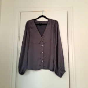 Blus från Lindex  - En jättefin åskblå/ grå blus från Lindex. Använd 2 gånger,  så gott som ny.  Köparen står för tillkommande fraktkostnad. Finns i Mjölby 