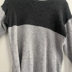 Stickad tröja  - Säljer min stickade tröja som är ljusgrå men även mörkgrå upp till. Den har två små slitsar på armarna.   Den är använd men syns inte. Vet tyvärr inte vart den kommer ifrån då den är ganska gammal