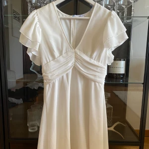 Studentklänning - Studentklänning/vit klänning från bubbelroom. Slutsåld. Lite blå bakom nacken av bandenden man får runt halsen, ej prövat tvätta bort