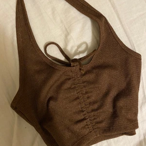 Croppad topp - Fin brun glittrig croptop från hm divided. Går att ändra längden med knytningen. Används inte, använd fåtal gånger, nyskick. Säljer då den är för liten. Nypris 50kr. Hör av dig vid frågor!
