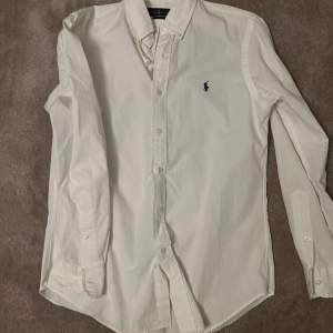 Klassisk grischig vit ralph lauren skjorta med blå logga. Denna skjorta är knappt använd och skick är 9/10. Nypris är 1700kr.