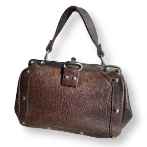 Vintageväska  - I fint skick för sin ålder, skinnet är lite slitet på vissa ställen. Syns på närbilderna! Medföljer ett axelband. MÅTT: Höjd 17cm, bredd 24cm & djup 10cm 