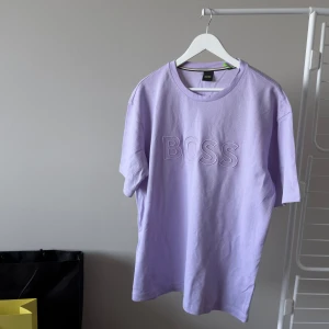 Brand New Hugo Boss Teecomfort T-shirt - Nyköpt från sommarkollektionen av Hugo Boss en pastell lila Teecomfort T-shirt med BOSS print. Oanvänd, Nypris 1045 kr. Material: 100% Bomull. Storlek: XL