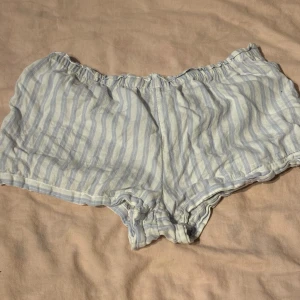 Randiga shorts från H&M - Säljer ett par supermysiga randiga shorts från H&M i storlek S. De är i en ljusblå och vit färgkombination och har en loose passform. Perfekta för varma sommardagar eller som loungewear hemma. De är i bomullsmaterial och har en elastisk midja för extra komfort. Skicket är bra och de är knappt använda.