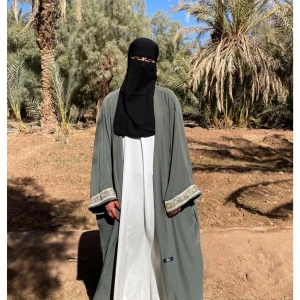 Grå abaya med spetsdetaljer - Säljer en elegant khaki öppen abaya med vackra spetsdetaljer på ärmsluten. Ärmarna har även knappar på insidan. Abayan är lång och har en lös passform, perfekt för både vardag och festliga tillfällen. Den är tillverkad i ett mjukt och bekvämt material som faller fint.