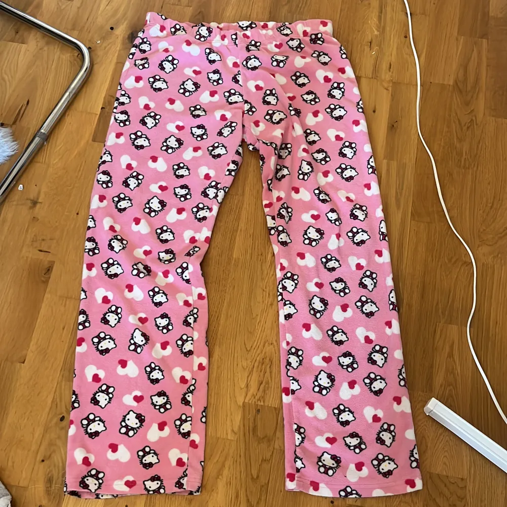 Ett par vintage rosa mjukisbyxor från Hello Kitty med ett mönster av Hello Kitty-figurer och hjärtan i vitt och rött. Byxorna har en elastisk midja och är tillverkade i ett mjukt och bekvämt material. Säljer då de inte passar! Fint skick. Jeans & Byxor.