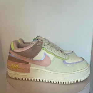 Nike Air Force 1 i pastellfärger - Säljer ett par Nike Air Force 1 sneakers i superfräscha pastellfärger. Skorna har en mix av beige, rosa, lila och gröna detaljer som gör dem riktigt unika. De är i nyskick och har en normal passform. Perfekta för vår och sommar!