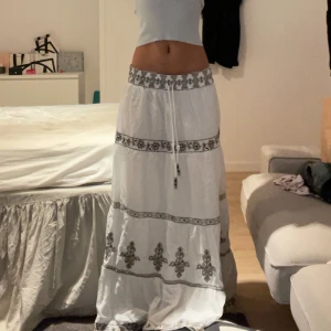 Vit långkjol med broderade detaljer - Säljer en superfin vit långkjol med snygga broderade detaljer i svart. Kjolen har en normal passning och är perfekt för sommaren. Den har ett knytband i midjan för justerbar passform. Passar perfekt till både vardag och fest! köpt från zara sommaren förra året använd fåtal gånger❤️