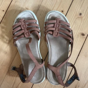 Bruna sandaler från Ecco - Säljer ett par bruna sandaler från Ecco i storlek 37. De är gjorda av skinn och har en snygg design med flera remmar och en justerbar spänne. Perfekta för sommaren!