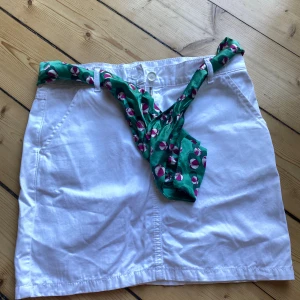 Vit kjol från Gucci med grönt bälte - Säljer en snygg vit kjol från Gucci i storlek xs. Kjolen har en normal passning och är tillverkad i bomull. Den har ett grönt bälte med ett mönster av vita och rosa detaljer som ger en fin kontrast. Perfekt för sommaren eller våren! 🥰
