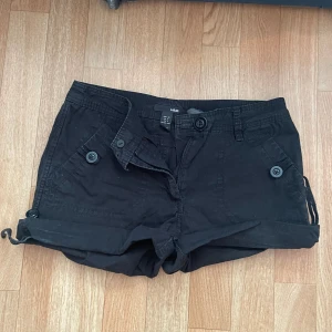 Svarta shorts från H&M - Ett par svarta shorts från H&M i storlek 36. Shortsen har knappar som detalj. De har fickor både fram och bak. Det går även att justera längden på den med spännerna på sidorna🤗