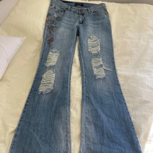 Lågmidjade utsvängda jeans - Skitsnygga lågmidjade bootcut jeans med slitningar och broderade blommor! Står storlek 40 så skulle säga typ M. 