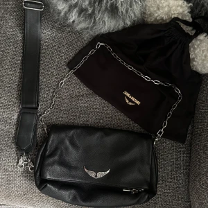 Zadig & Voltaire väska  - Väska från Zadig & Voltaire i modellen Rocky!  Väskan är i väldigt fint skick och köptes på NK i Gbg, medföljande dustbag och kvitto finns kvar! Bredd x Höjd x Djup: 27 x 16 x 12 cm.  Justerbar axelrem: 70 cm - 115 cm. Kedjeremmens längd: 29 cm.