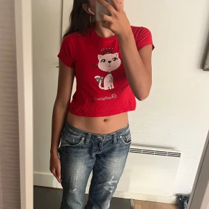 Röd croppad t-shirt med kattmotiv från Fruit of the Loom - Säljer en supergullig röd t-shirt från Fruit of the Loom. Den har ett sött kattmotiv med en krona och är i väldigt bra skick utan tecken på användning!