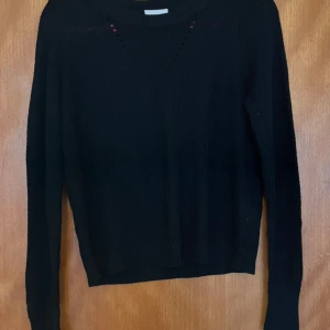 Svart stickad tröja från VILA - Säljer en svart stickad tröja från VILA i storlek XS. Tröjan har ett mönster med små hål vid halsringningen. Den är långärmad och och i stumt material. Katt finns i hemmet, men allt jag säljer är nytvättat och rollat ✨