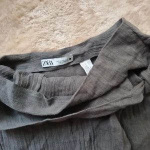 Grå långklänning från Zapa - En elegant grå långkjolfrån Zara. Kjolen har en lös passform och är tillverkad av ett mjukt och bekvämt material. Perfekt för både vardag och strandtillfällen.