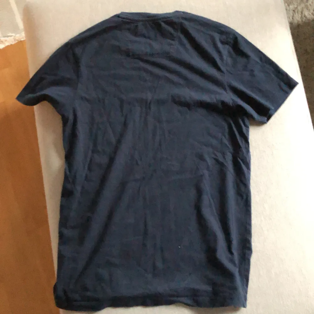 En mörkblå t-shirt från Ben Sherman med ett grönt och grått mönster av Union Jack-flaggan på framsidan. T-shirten har korta ärmar och en normal passform. Tröjan har aldrig använts och är i nyskick. Säljs billigt då jag vill bli av med det!. T-paidat.