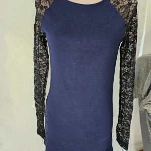 Mörkblå klänning från H&M Divided - En elegant mörkblå klänning från H&M Divided med spetsdetaljer på ärmarna och axlarna. Klänningen har en dragkedja på baksidan och är långärmad.