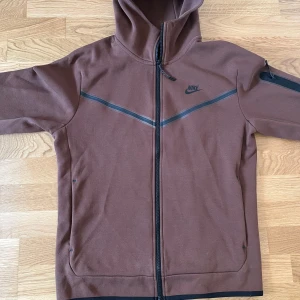Brun Nike tech fleece - Hej säljer min bruna Nike tech fleece eftersom jag använder inte den längre. Väldigt bra skick har bara haft på mig den 3-4 gånger annars inte använt. Storlek M men passar S också. Helt original, köpt från JDsports för 1500kr. Går att ta fler bilder.