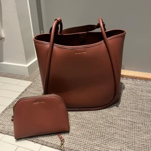 Brun väska - Brun väska från märket Charles & Keith i nyskick! Tillhörande necessär. Köpt i Singapore! Hör av er vid frågor! Kan mötas upp då väskan är ganska stor att frakta! 