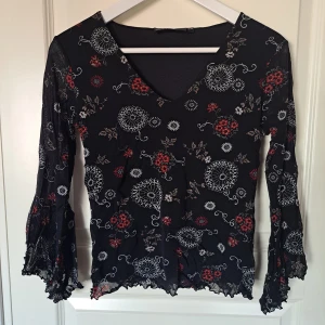 Mönstrad svart blus - Svart mönstrad blus med röda och vita detaljer med glitter. Tröja har vida ärmar. Thriftad från KappAhl i storlek 38/40