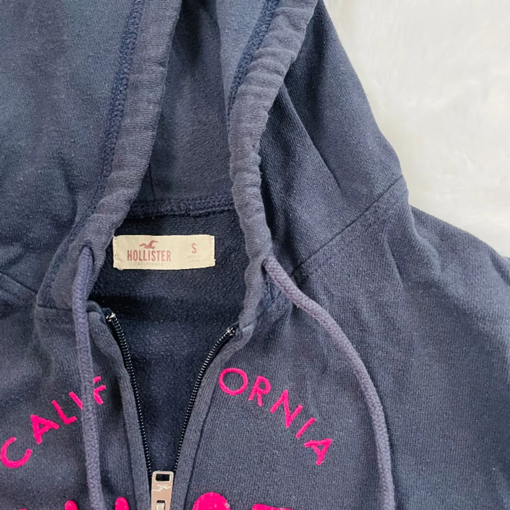 Säljer en marinblå hollister tröja med rosa tryck, luva och dragkedja. Använd men fint skick. Köpt i hollister butik. Säljer billigt och kollar intresse istället för att det slängs🦋. Hoodies.