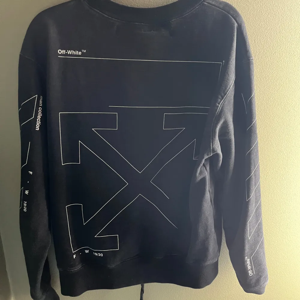 Svart sweatshirt med vita detaljer. Tryck på fram och baksida. På ärmarna står det 