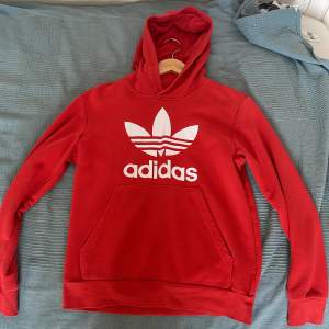 En röd hoodie från Adidas med vit logotyp på framsidan. Hoodien har en stor ficka på magen. Den är långärmad och har ribbstickade muddar vid ärmslut och nederkant. Jag köpte den för 700kr och säljer den nu för 250kr