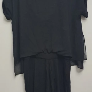 Svart klänning från Zara - En elegant svart klänning från Zara med ett transparent yttre lager och en underklänning. Klänningen har korta ärmar och en lös passform.