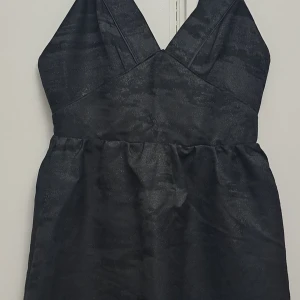 Svart klänning - En elegant svart klänning med breda axelband och en djup V-ringning. Klänningen har en åtsittande överdel och en något utsvängd kjol.