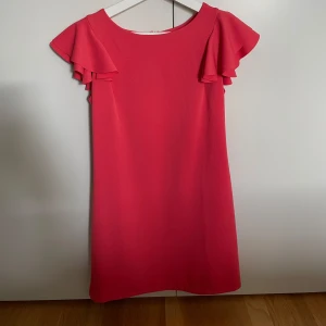 Volang sommarklänning - En rosa klänning med volangärmar. Klänningen är figursydd och har en rund halsringning. Den har en dold dragkedja i ryggen. Motsvarar till storlek S. Använd vid 1 tillfälle, som ny. Köpte utomlands.