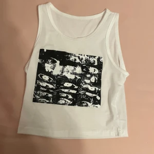 Vit linnetopp med svart tryck - En vit linnetopp med ett svart tryck av ögon på framsidan. Toppen är ärmlös och har en rund halsringning. Skriv gärna om ni har frågor 💕