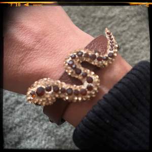 Brunt armband i skinnimmitation med orm i guld och gula stenar. Knappt använt. 22,5 cm x 1,2 cm