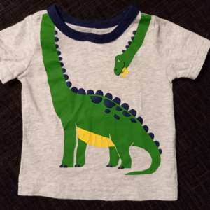 Gråmelerad t-shirt med en dinosaurie i storlek 6 mån (ca strl. 68) från Carter's. I mycket fint skick, ser oanvänd ut. Inga hål eller fläckar, helt tryck.   Tvättad i parfymfritt tvättmedel och utan sköljmedel. 