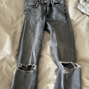 Grå jeans  - Gråa jeans från zara slitningar i knäna och slits längst ner. 