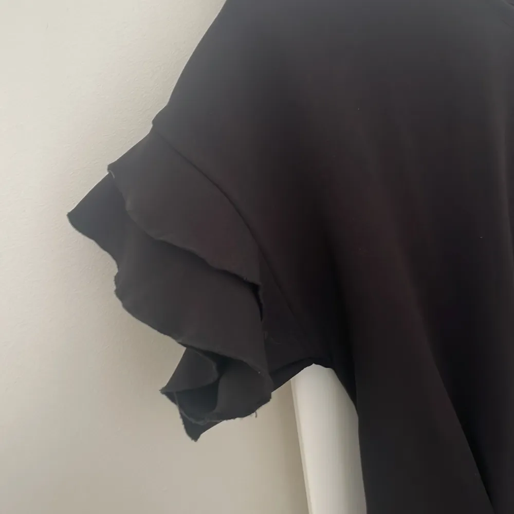 En svart kortärmad blus i fint material med volanger vid ärmarna. Knappt använd.. Puserot.