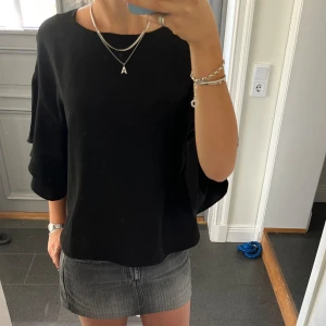 Svart volangtopp - Svart blus/topp med volanger från H&M i storlek 38. Fint skick. Använd gärna köp nu!