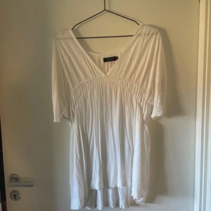 Vit blus från Sense Woman - En vit blus från Sense Woman med v-ringning och korta ärmar. Blusen har en rynkad detalj under bysten och är tillverkad i ett lätt och luftigt material.