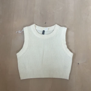  stickad topp  - En vit stickad topp från Divided. Toppen är ärmlös och har en ribbad struktur. Den är croppad och har en rund halsringning. bra skick dock en liten defekt (se bild 4)