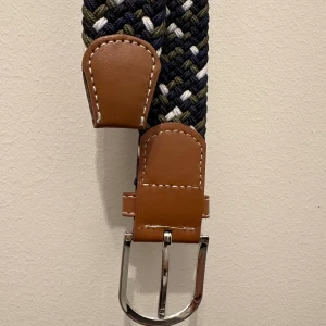 Flätat bälte  - Bältet är i mycket bra skick och helt oanvänt det är också riktigt snyggt. Färgerna på bältet är vitt, blått och grönt sicksack mönster.
